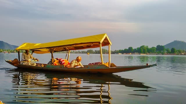 A wooden shikara gliding across Dal Lake with the mountains of Srinagar beyond